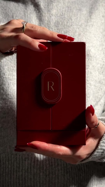 A close-up shot focusing on hands presenting a minimalist red gift box with a prominent gold logo, highlighting the anticipation of a jewelry reveal.