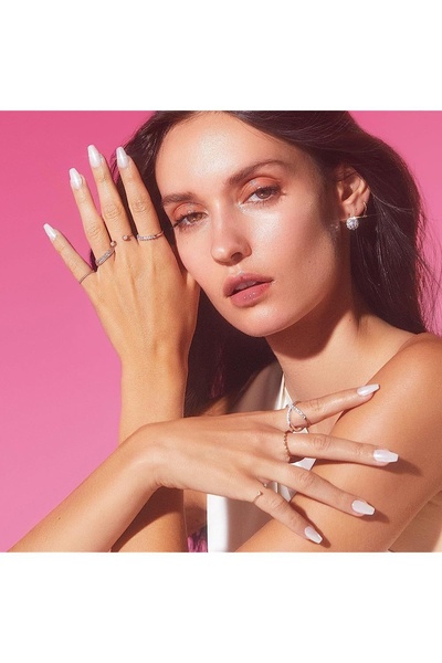 A close-up studio shot of a hand model wearing multiple gold rings against a vibrant pink background, emphasizing jewelry detail and luxury mood.