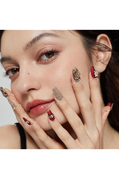 A close-up portrait of a model showcasing intricate press-on nails with a matte finish and embellishments, emphasizing texture and luxury.