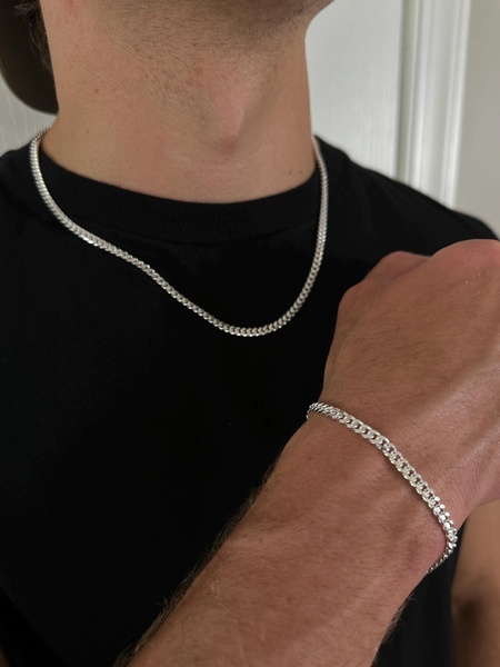 A close-up, high-contrast shot showcasing a silver chain necklace and matching bracelet on a model to emphasize fit and material luster.