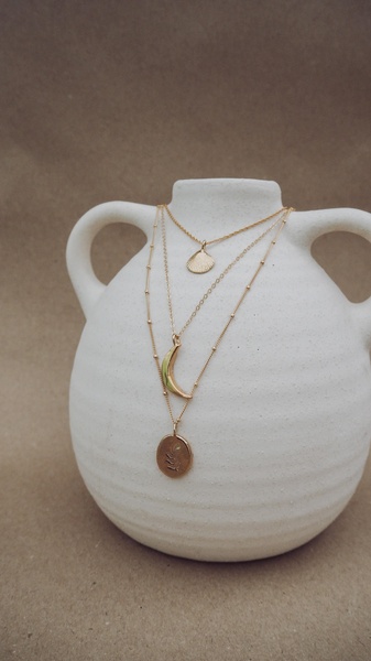 A vertical-oriented close-up shot featuring a delicate layered necklace set draped over an off-white ceramic vase against a textured, neutral background.