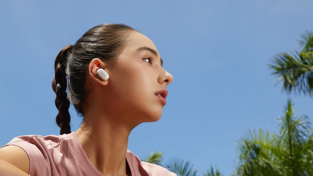 A close-up profile shot of a person wearing minimalist white wireless earbuds outdoors against a clear blue sky, emphasizing a clean and premium lifestyle aesthetic.