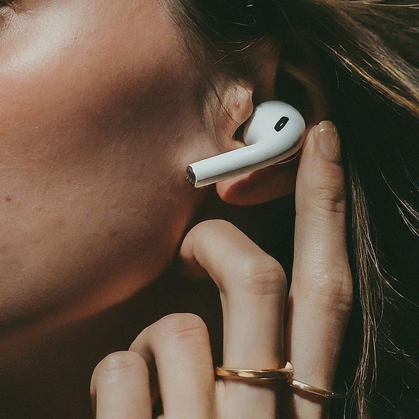 A high-contrast, lifestyle-focused close-up of a person using a white wireless earbud, highlighting the product as an everyday essential.