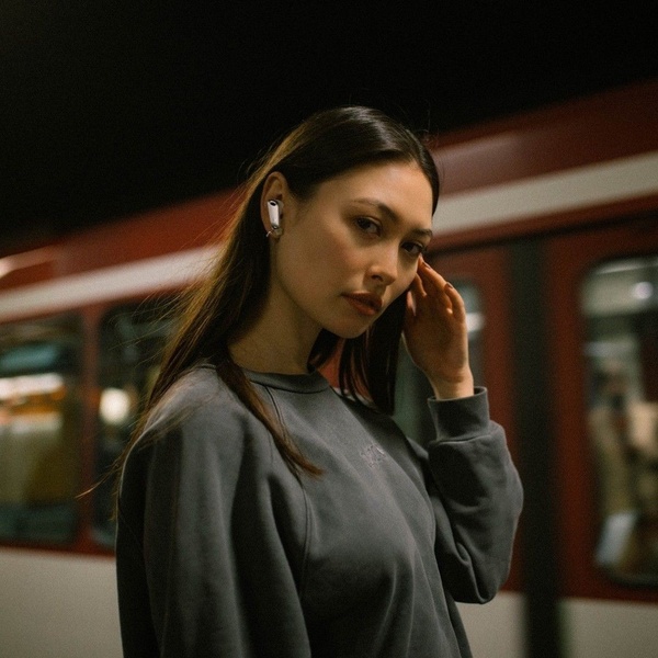 A high-contrast, moody portrait of a woman wearing wireless earbuds in a transit station, emphasizing a modern lifestyle aesthetic.