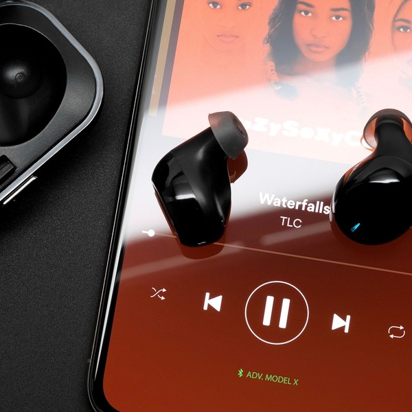 A close-up, high-contrast shot of wireless earbuds placed on a smartphone screen that shows a music player interface.