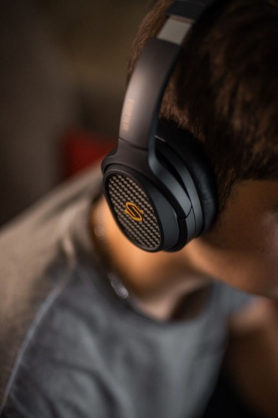 A close-up shot focused on the ear cup of premium headphones, highlighting the carbon fiber material and brand logo.