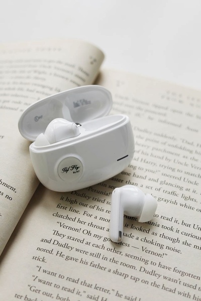 A clean, high-angle product photograph of white wireless earbuds in their open case, placed directly on an open book.