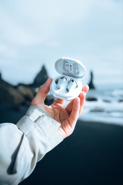 A high-quality product hero shot featuring wireless earbuds inside their charging case held against a blurred, moody coastal cliff landscape.