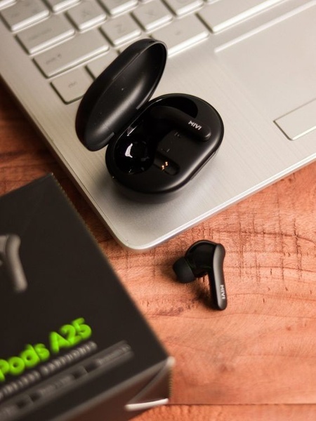 A clean, high-angle product shot of wireless earbuds in their charging case placed on a laptop, paired with the product packaging.
