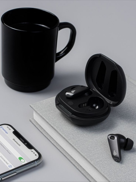 A high-contrast, minimalist tabletop setup featuring wireless earbuds, a mobile device, and a black coffee mug, shot in a 3:4 ratio for mobile feeds.