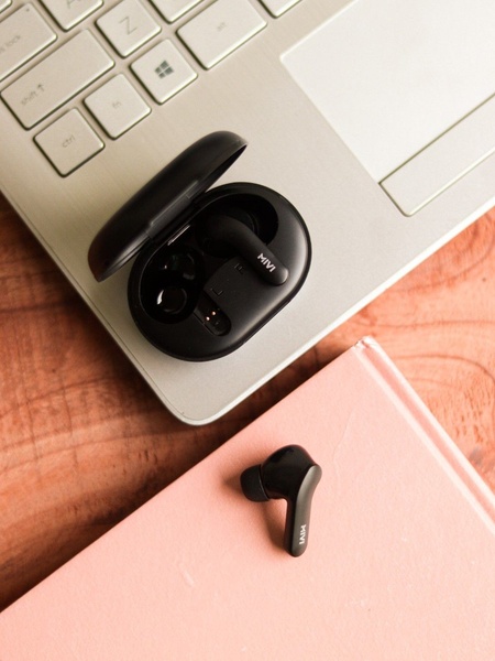 A top-down view of wireless earbuds resting on a laptop and a soft pink notebook, emphasizing a clean, organized desk aesthetic.