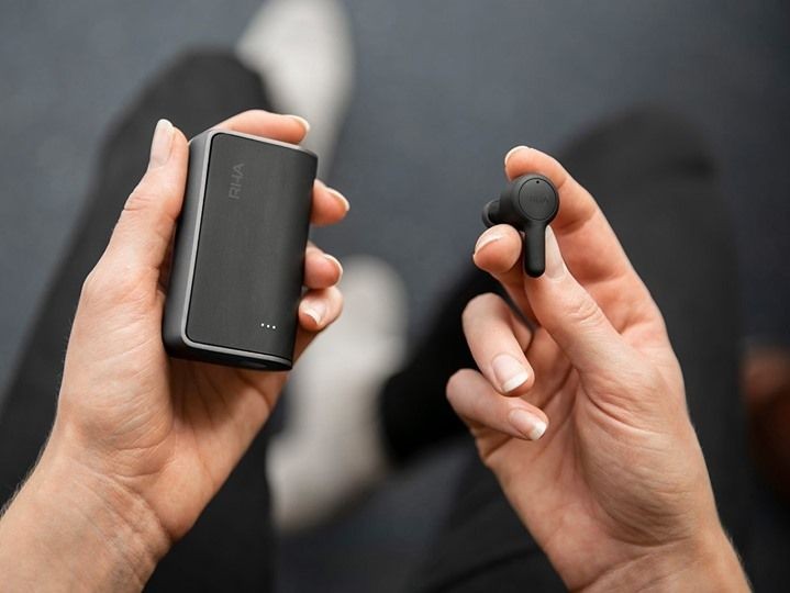 A close-up, top-down shot of a person holding wireless earbuds and their charging case, emphasizing the sleek, black design against a neutral background.