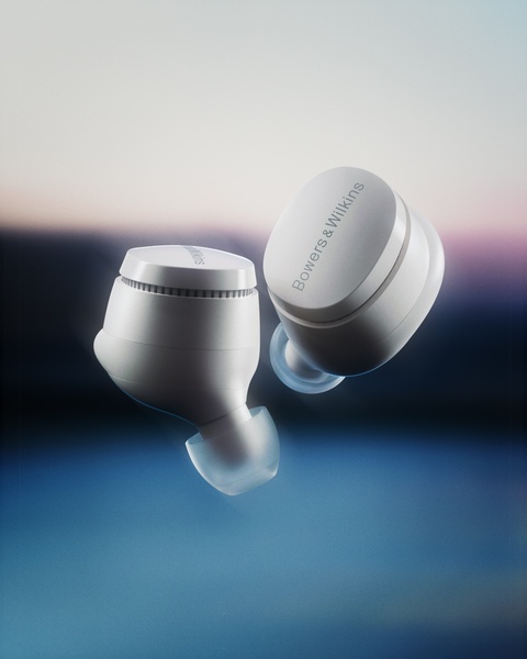 A high-end, clean product photography shot of wireless earbuds floating against a soft-focus, sunset-toned background.