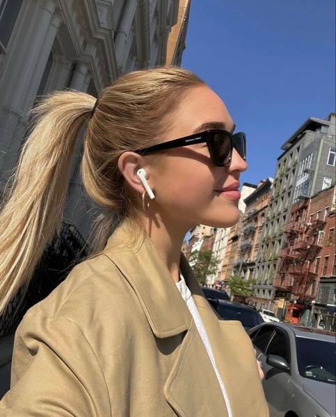 A close-up side profile of a woman wearing wireless earphones in a city setting, capturing a natural, high-end lifestyle aesthetic.