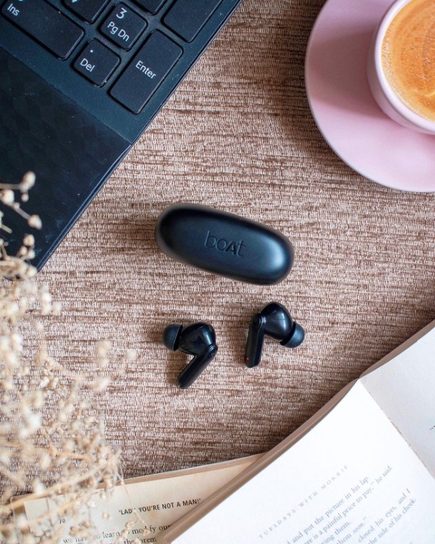 A high-angle, aesthetic shot featuring wireless earbuds and their charging case set against a textured, neutral background with a laptop and coffee.