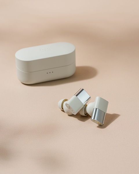 A clean, studio-lit shot of wireless earbuds and their charging case on a soft beige background, emphasizing premium materials and minimalist design.