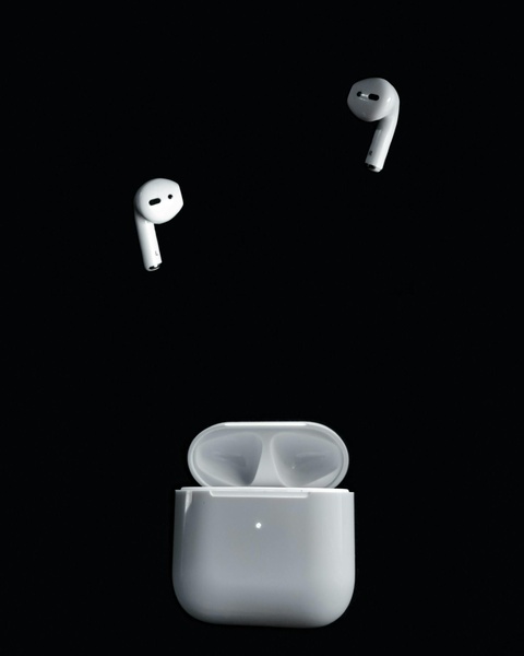 A high-contrast, studio-style product shot featuring white wireless earbuds floating above their charging case against a stark black background.