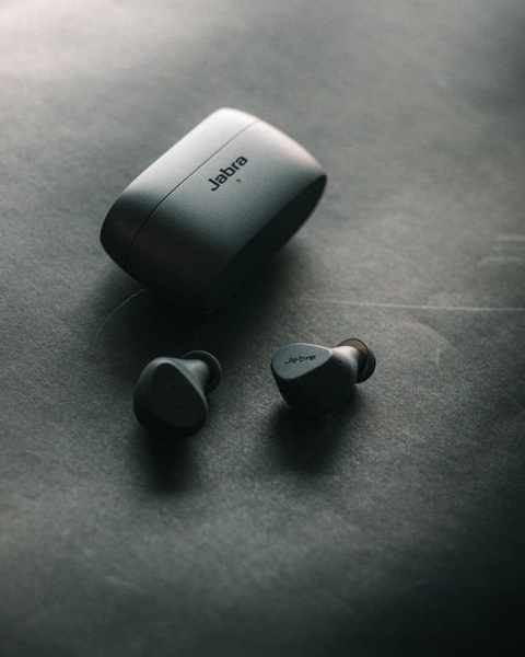 A high-contrast, professional product photograph featuring wireless earbuds and their charging case on a dark, textured background.