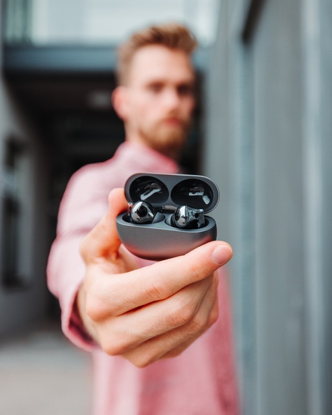 A close-up, first-person perspective of a hand presenting wireless earbuds in their charging case, creating an intimate and immediate product focus.