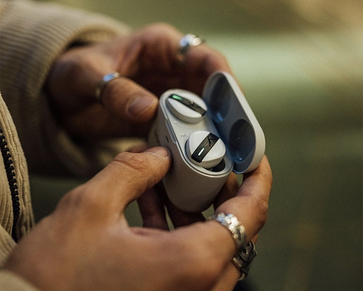 A close-up shot focusing on hands holding a wireless charging case for earbuds, emphasizing the product's design and texture in a natural, warm-toned environment.