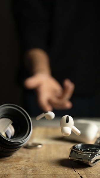 A high-end, minimalist product shot featuring wireless earbuds floating in mid-air against a blurred background with professional photography equipment.