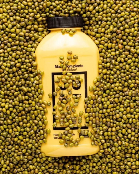 A top-down, high-contrast shot of a yellow liquid egg bottle centered in a field of green mung beans.