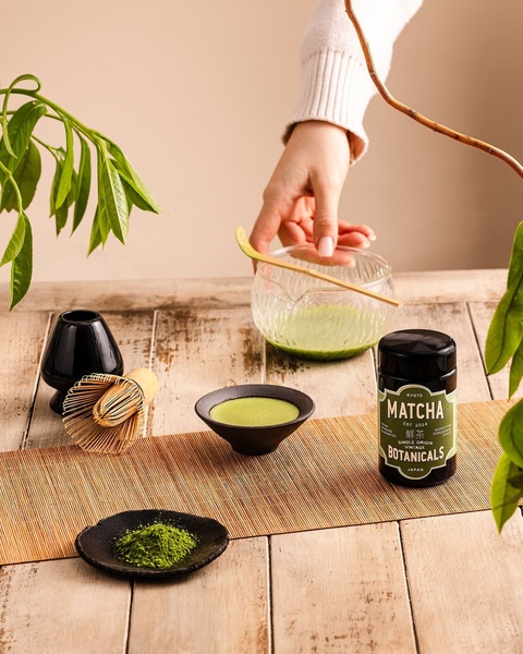 A top-down, serene product hero shot featuring premium matcha powder, a bamboo whisk, and a ceramic bowl in a natural lighting setting.