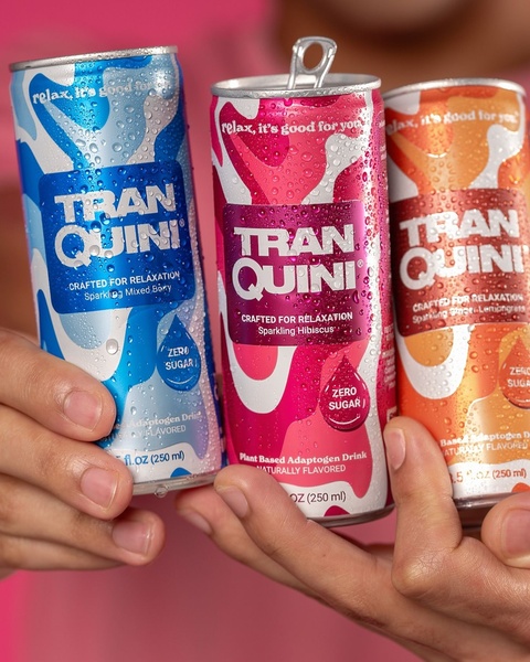A close-up shot showing three colorful cans of sparkling adaptogen drink, each held by a person against a bright, matching background.