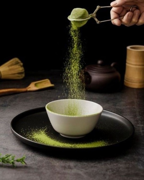 A high-contrast hero shot of matcha powder being sifted into a ceramic bowl, emphasizing freshness and quality through natural textures.