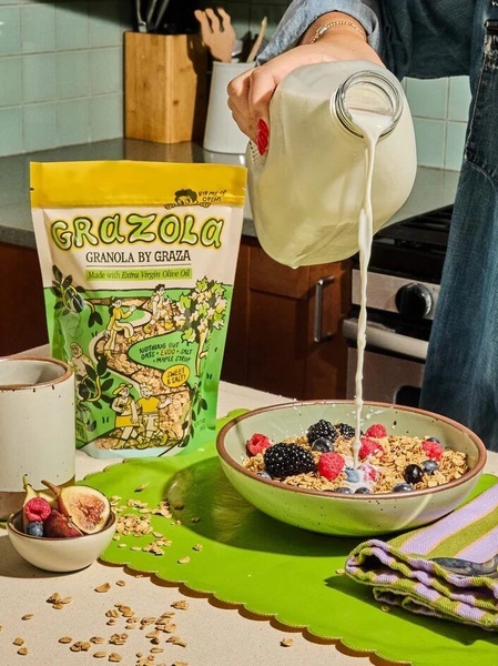 An authentic, high-contrast shot of milk being poured into a bowl of artisanal granola, featuring the product packaging clearly displayed alongside fresh ingredients.