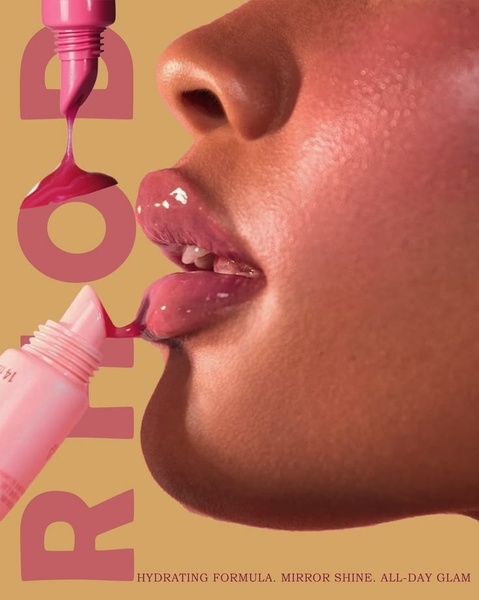 A close-up, high-definition shot showing lip gloss being applied to lips, highlighting the texture and mirror-shine finish of the product.