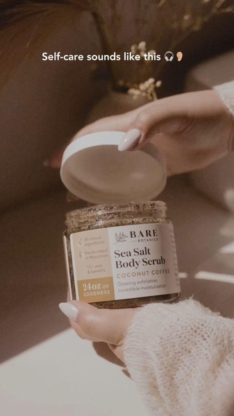 A close-up, warm-toned image of a Sea Salt Body Scrub jar being opened, emphasizing a luxurious and sensory self-care experience.