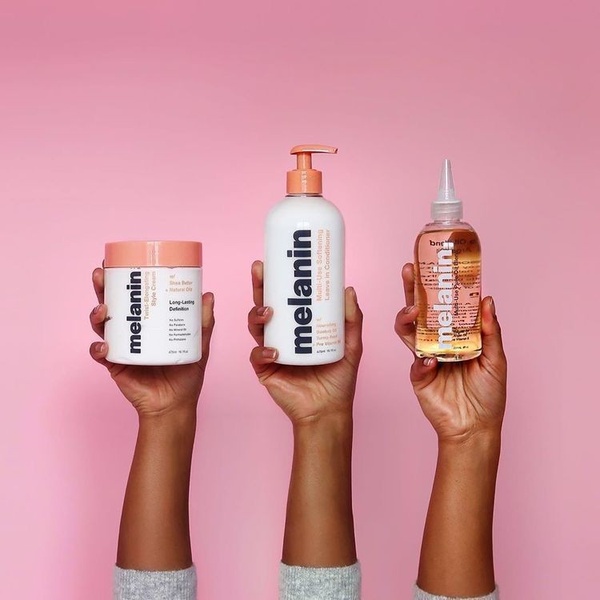 A clean, studio-lit photograph featuring three hair care products held up against a solid pink background.