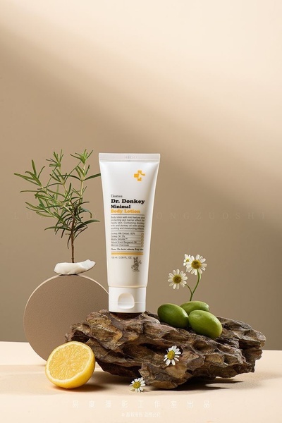 A high-quality product photography shot featuring a tube of body lotion surrounded by natural elements like lemons and daisies on a wooden base.