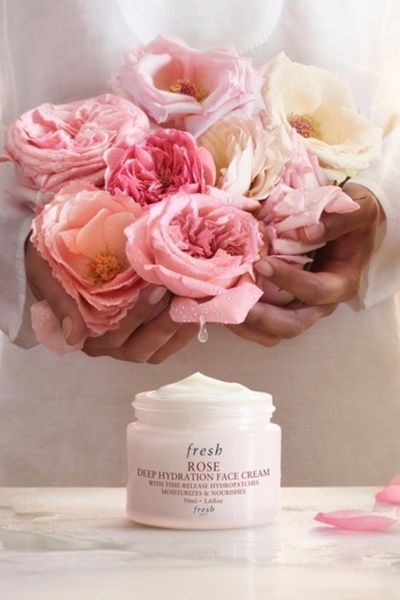 A delicate, high-end product hero shot featuring a jar of face cream held with fresh roses in soft, natural lighting.