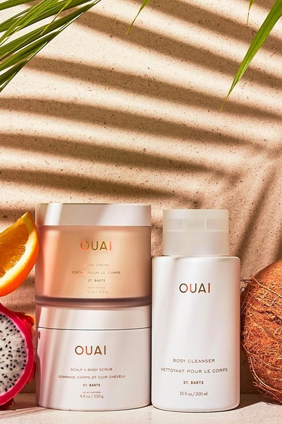A high-end, aesthetic still life featuring three body care products arranged with fresh citrus and coconut against a textured, sun-drenched backdrop.