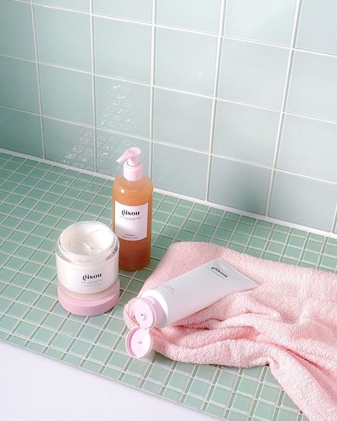 A high-quality, clean product shot of hair care essentials placed on a mint green tiled surface with a soft pink towel, evoking a spa-like mood.