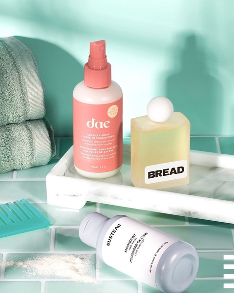 A high-key, bright product display featuring three different hair care bottles arranged on a white marble tray with a matching comb and towels.