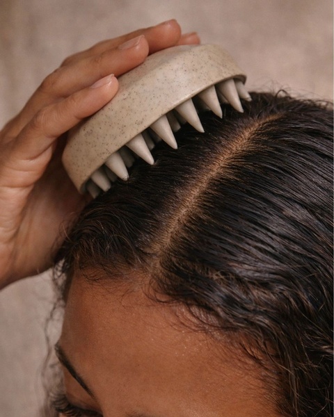 A close-up, high-quality image of a hand using a silicone scalp massager on wet hair to demonstrate immediate product application.