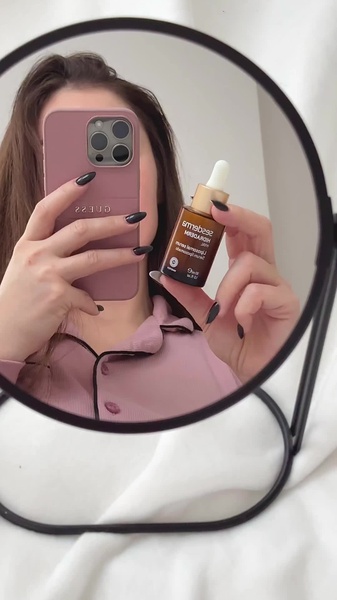 A casual, user-generated style shot featuring a person holding a bottle of liposomal serum in a mirror, maintaining a grounded and authentic aesthetic.