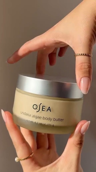 A close-up, high-quality shot of a person holding an Undaria Algae Body Butter jar, focusing on clean lighting and product presentation.