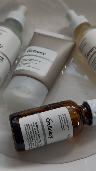 A top-down, clean product shot of various skincare bottles and creams arranged on a white, water-drenched surface to emphasize purity and hydration.