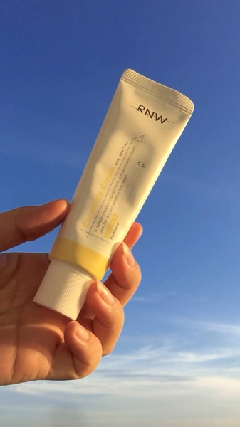 A high-contrast, sunlit, close-up shot of a ceramide cream tube held against a clear blue sky, emphasizing product purity and simplicity.