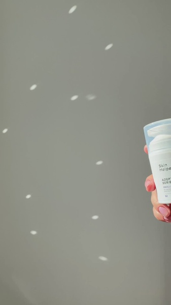 A close-up aesthetic shot of an emulsion bottle being held against a soft grey background with dappled sunlight effects.