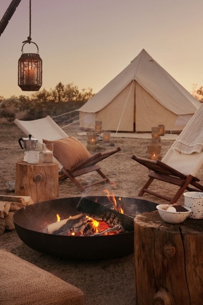 This creative showcases a luxury canvas bell tent at dusk, surrounded by warm lanterns, campfire seating, and an inviting, serene outdoor atmosphere.