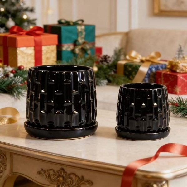 A elegant studio-style hero shot featuring two black textured ceramic planters on a luxury table against a background of festive holiday gifts.