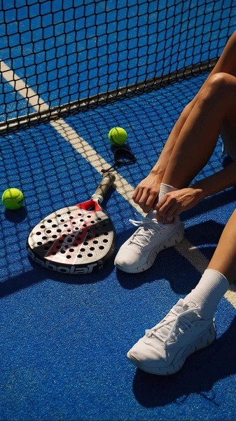 A close-up shot of a player preparing for a match on a bright blue padel court, highlighting the equipment and the athletic lifestyle.