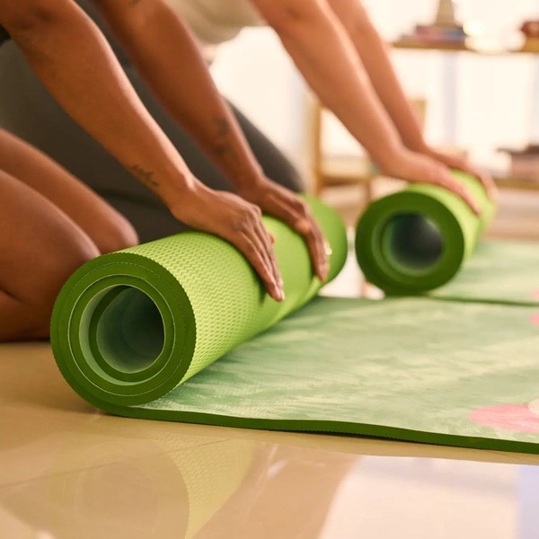 A close-up shot capturing two individuals rolling out vibrant green yoga mats, emphasizing the physical experience and quality of the product.