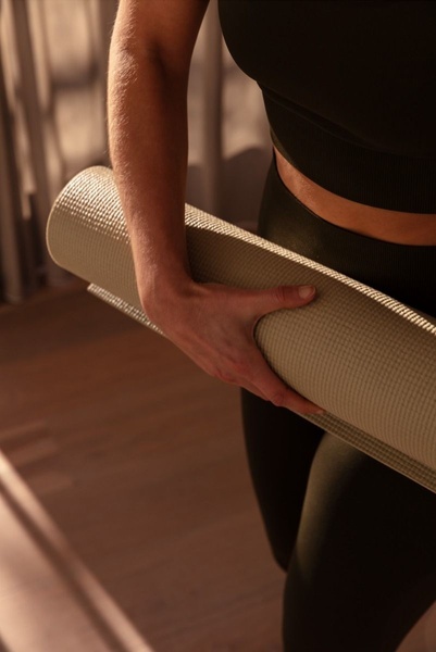 A close-up, cropped shot focusing on the texture and quality of a rolled yoga mat held by a model in athletic wear, emphasizing a clean and serene brand atmosphere.