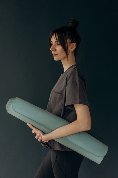 A high-quality studio portrait featuring a model holding a sage green yoga mat against a dark background, emphasizing a clean and aspirational brand aesthetic.